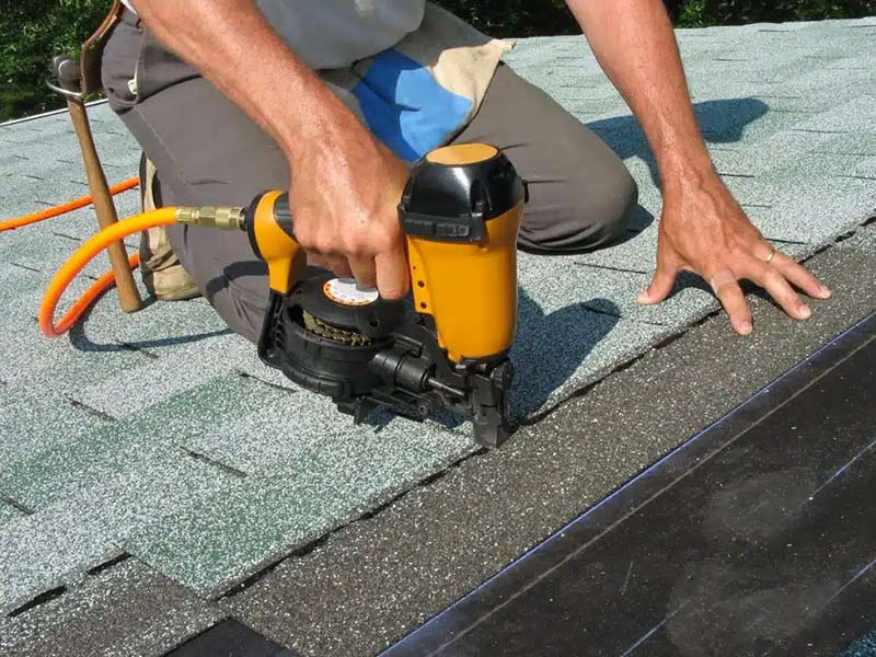Man using nail gun to apply asphalt shingles
